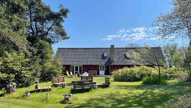 Un bâtiment rouge avec un toit en pente, entouré d’une zone herbeuse où se trouvent des bancs en bois et une boîte aux lettres.