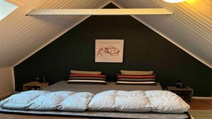 Une chambre de style « loft », avec un plafond en pente, un lit agrémenté de plusieurs coussins, une œuvre d’art encadrée au mur et une petite table avec une lampe.