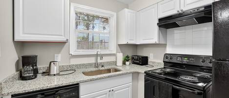 A kitchen with white cabinets, a black stove, and a granite countertop.