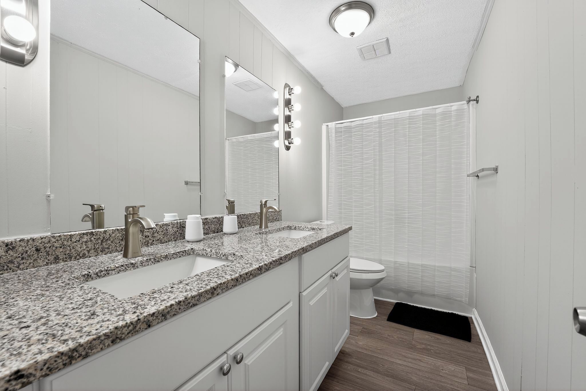A bathroom with a granite countertop sink, a large mirror, and a shower curtain.