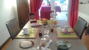 Una mesa de comedor dispuesta con platos, cubiertos y condimentos, con vistas a un patio al fondo.