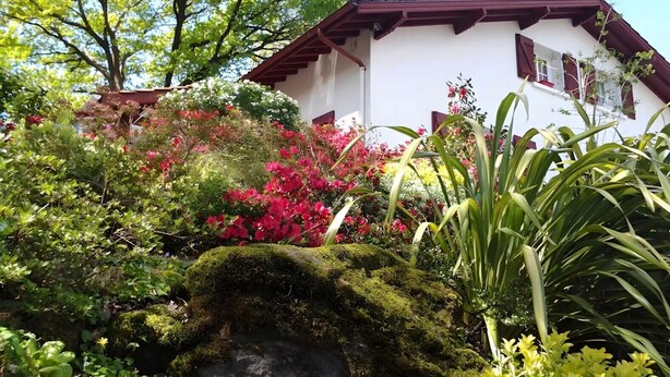 Un edificio blanco con tejado rojo y un jardín con diversas plantas y flores.