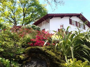 Un edificio blanco con tejado rojo y un jardín con diversas plantas y flores.