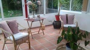 Una habitación con sillas de mimbre, una mesita, una planta en maceta y vistas por la ventana.