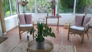 Una habitación con dos sillas de mimbre, una mesita, una planta en maceta y un tapete estampado.