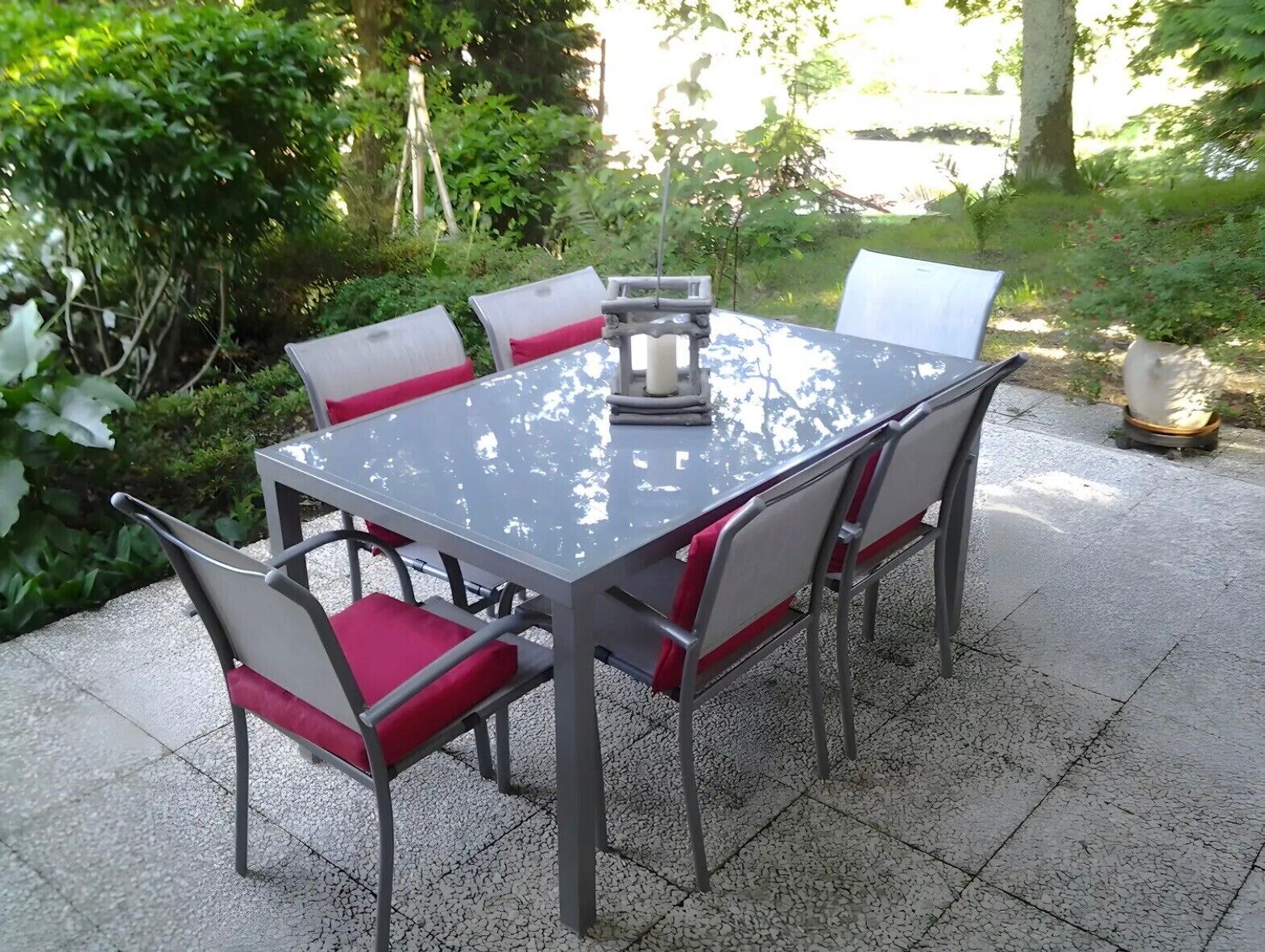 A rectangular outdoor table with a metal frame and red cushioned chairs.