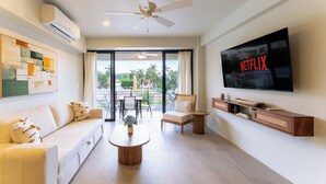 Een moderne woonkamer met een flatscreentelevisie, plafondventilator en een groot raam met uitzicht op een balkon.