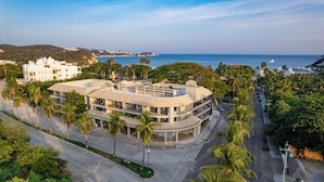 Een modern hotel met een gebogen gevel, palmbomen en uitzicht op zee.