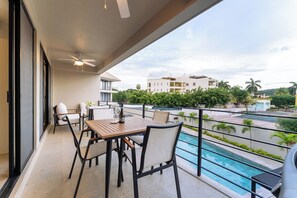 Un balcon avec une table et des chaises, une piscine et une vue sur les bâtiments et la verdure.