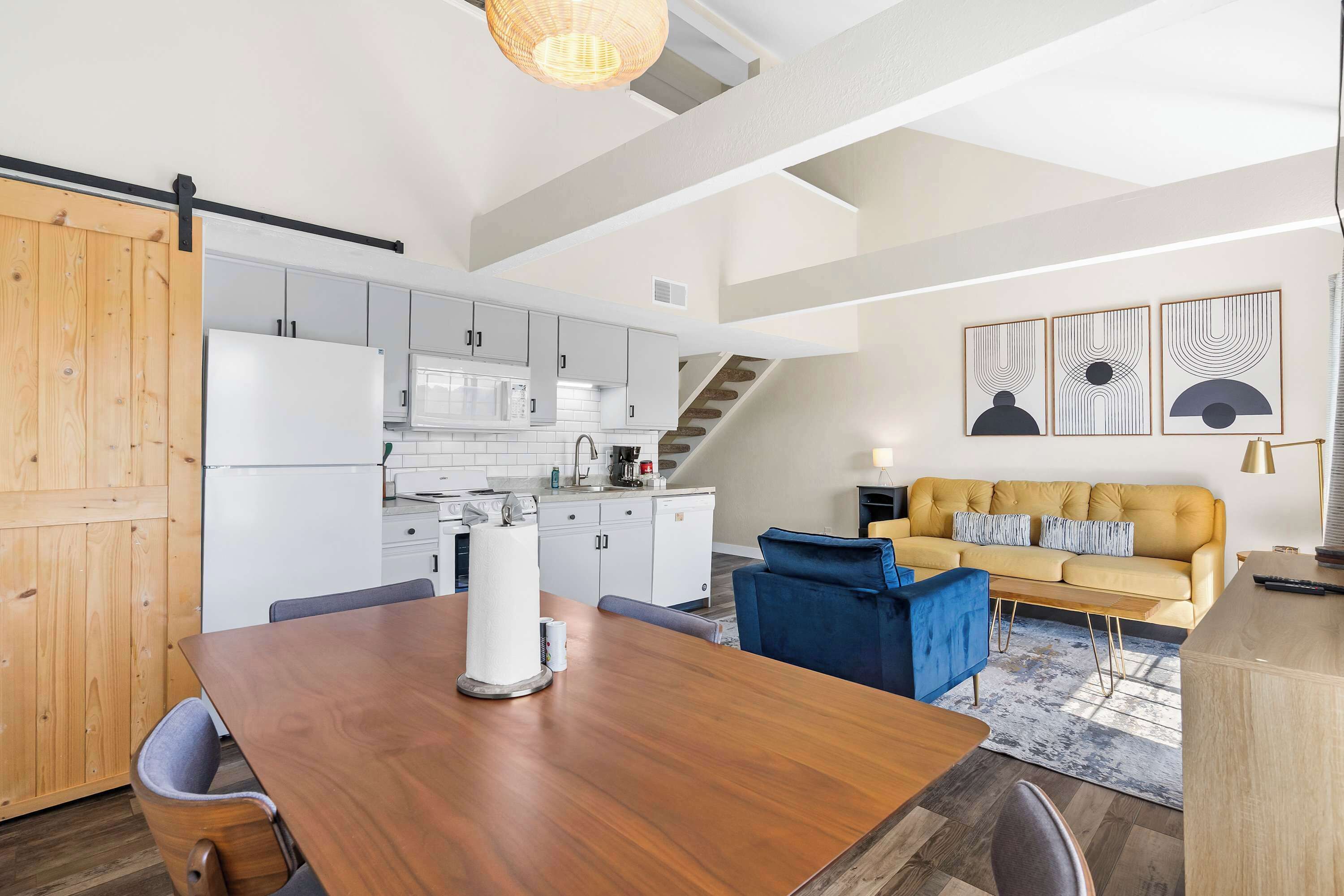 A modern kitchen with white cabinets, a wooden dining table, and a blue sofa in the living area.