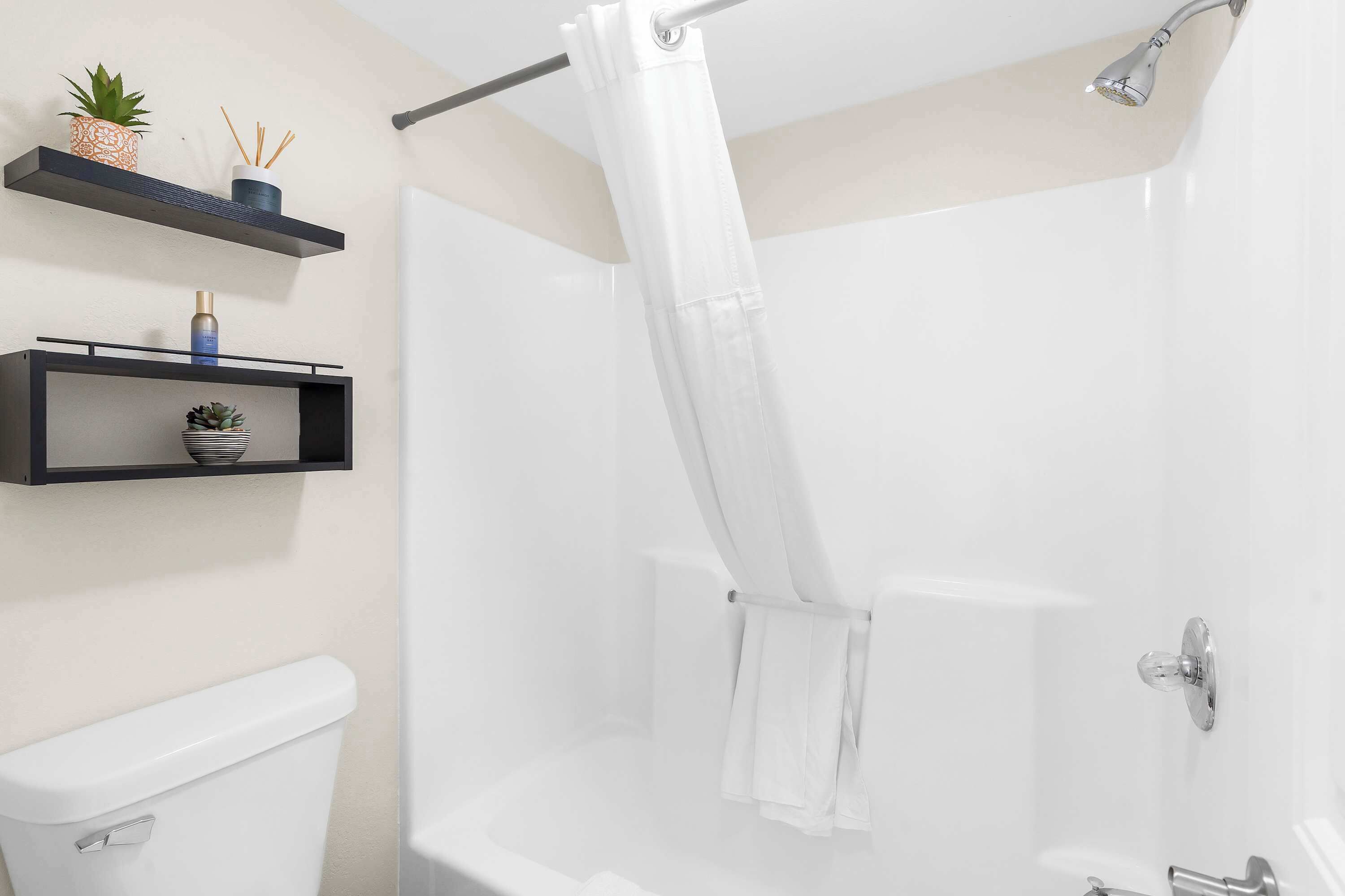 A modern bathroom with a white bathtub, a shower curtain, and two black shelves with decorative items.