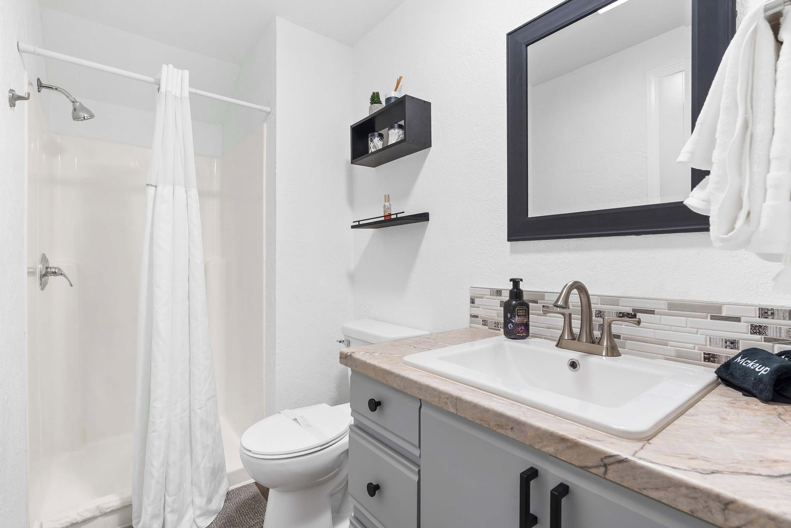 A bathroom with a shower, toilet, sink, and a mirror.