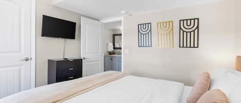 Habitación de hotel con cama, televisor montado en la pared, cómoda y obras de arte decorando la pared.