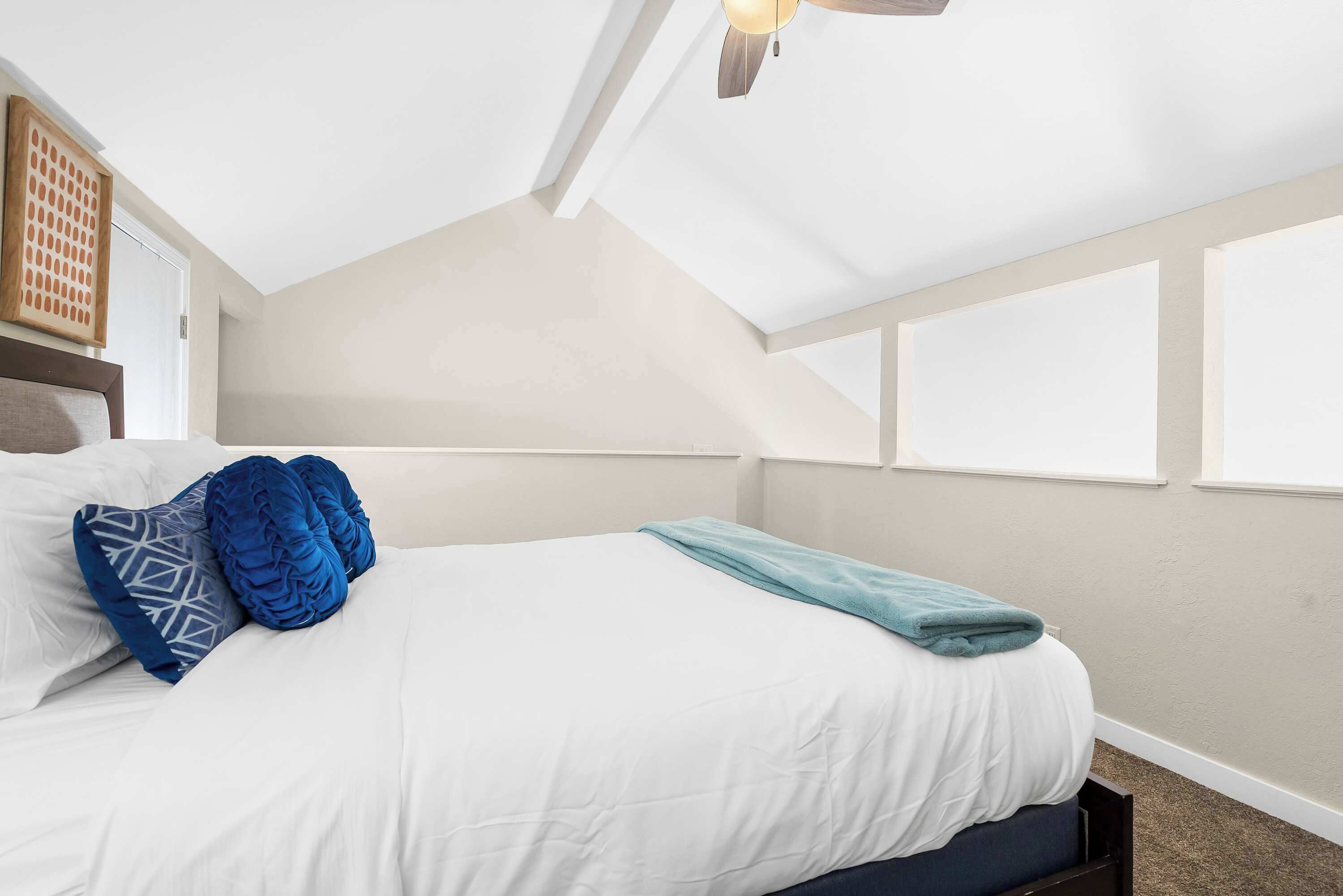 Een slaapkamer met een bed, kussens, een plafondventilator en ramen.