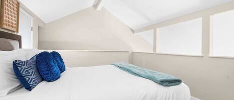 A bedroom with a bed, pillows, a ceiling fan, and windows.