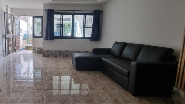 A spacious living room with a black leather sofa, a large window with curtains, and a tiled floor. - Chiang Mai Oasis 2-bedroom Home With Private Entrance & Modern Amenities (Chiang Mai)