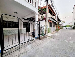 A residential street with houses, a gated entrance, and parked cars. - Chiang Mai Oasis 2-bedroom Home With Private Entrance & Modern Amenities (Chiang Mai)