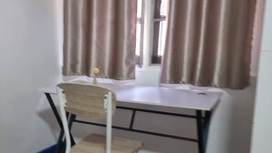 A corner room with a desk and chair, a window with curtains, and a blue baseboard. - Chiang Mai Oasis 2-bedroom Home With Private Entrance & Modern Amenities (Chiang Mai)