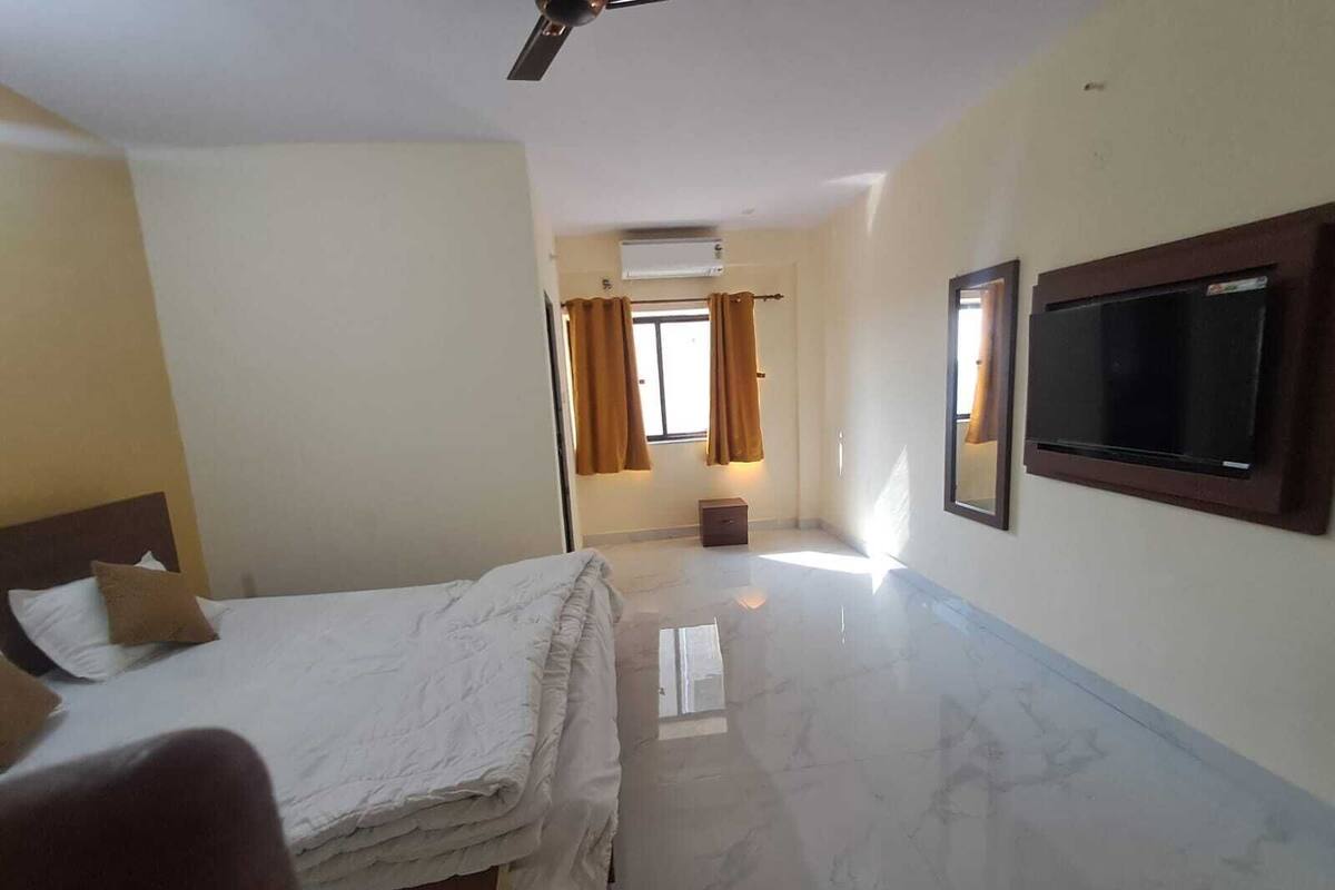 Quarto de hotel com uma cama, televisão, ventoinha no teto e janela com cortinas.