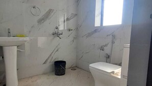 A bathroom with a marble floor, a white sink, a toilet, and a window. - Keshav Inn Hotel And Banquet (Ranchi)