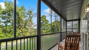 A covered porch with a view of a wooded area, featuring two wooden chairs and a table. - The Fairway Getaway For 6 (Branson West)