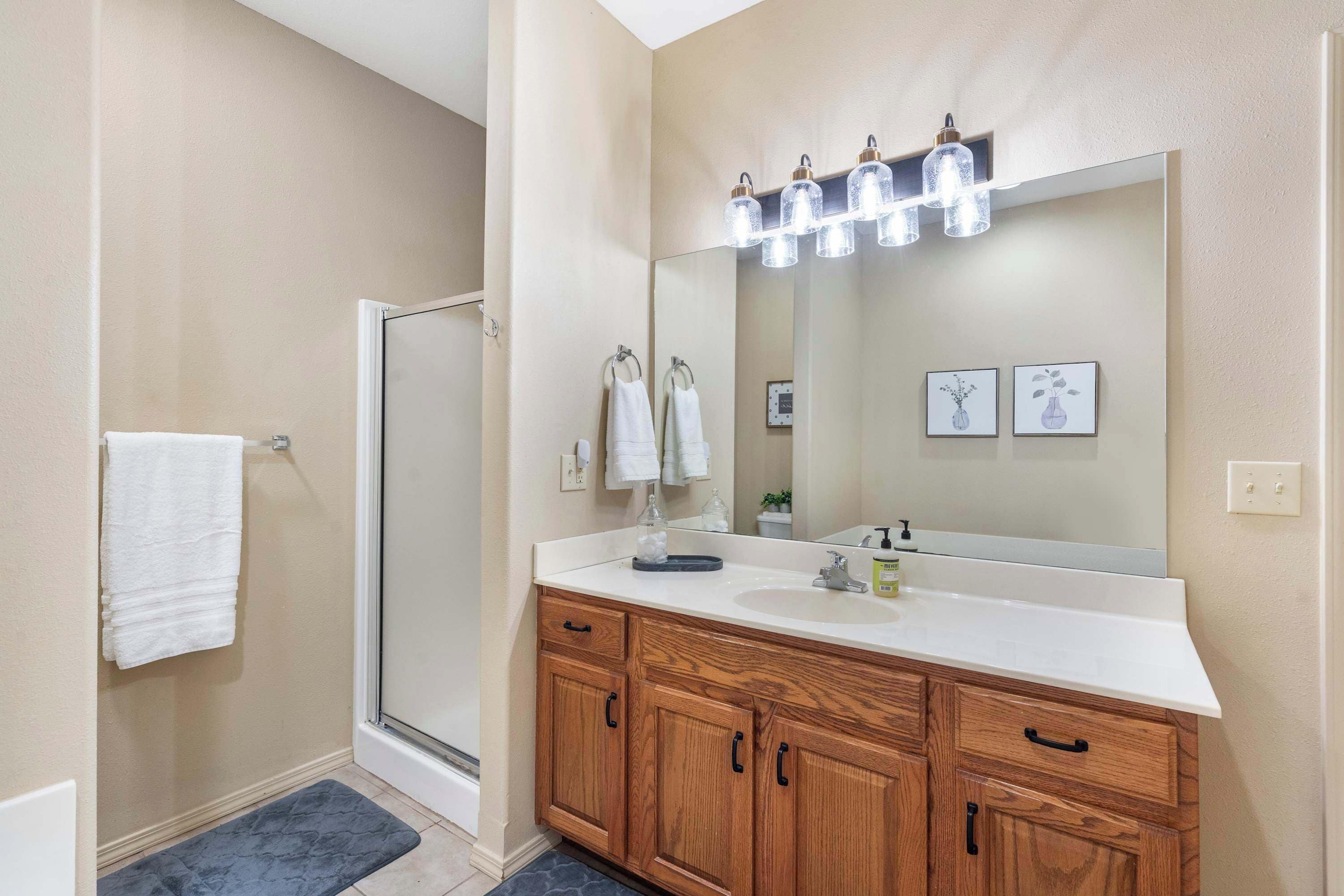 A modern bathroom with a glass shower door, wooden vanity, and a large mirror with lights.