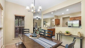 A dining room with a wooden table, chairs, and a chandelier. There is a kitchen area with wooden cabinets and a refrigerator. - The Fairway Getaway For 6 (Branson West)
