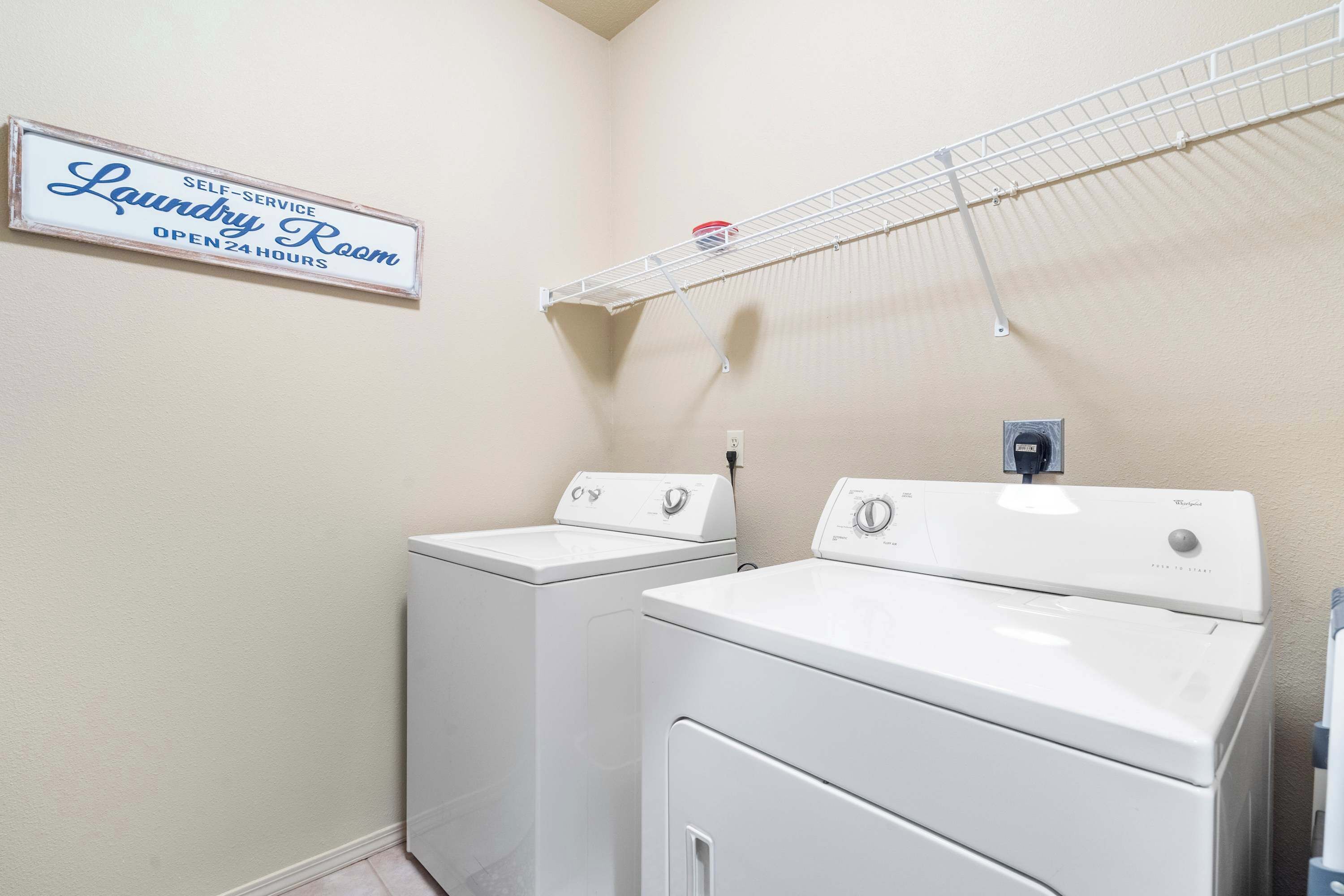 A self-service laundry room with two washers and dryers, a drying rack, and a sign indicating 24-hour availability.