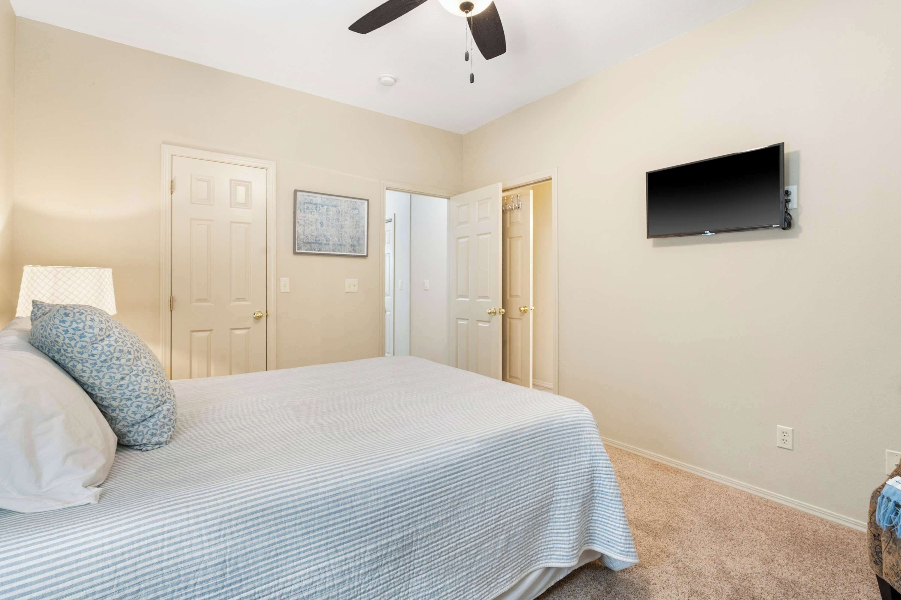 Un dormitorio con cama, ventilador de techo, televisor montado y dos puertas.