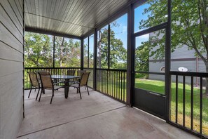 Une terrasse couverte avec une table et des chaises, de grandes fenêtres et une vue sur une pelouse.