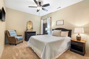 Une chambre à coucher comprenant un lit, une chaise, une table de chevet, un ventilateur de plafond, un miroir et un panneau affiché sur le mur.