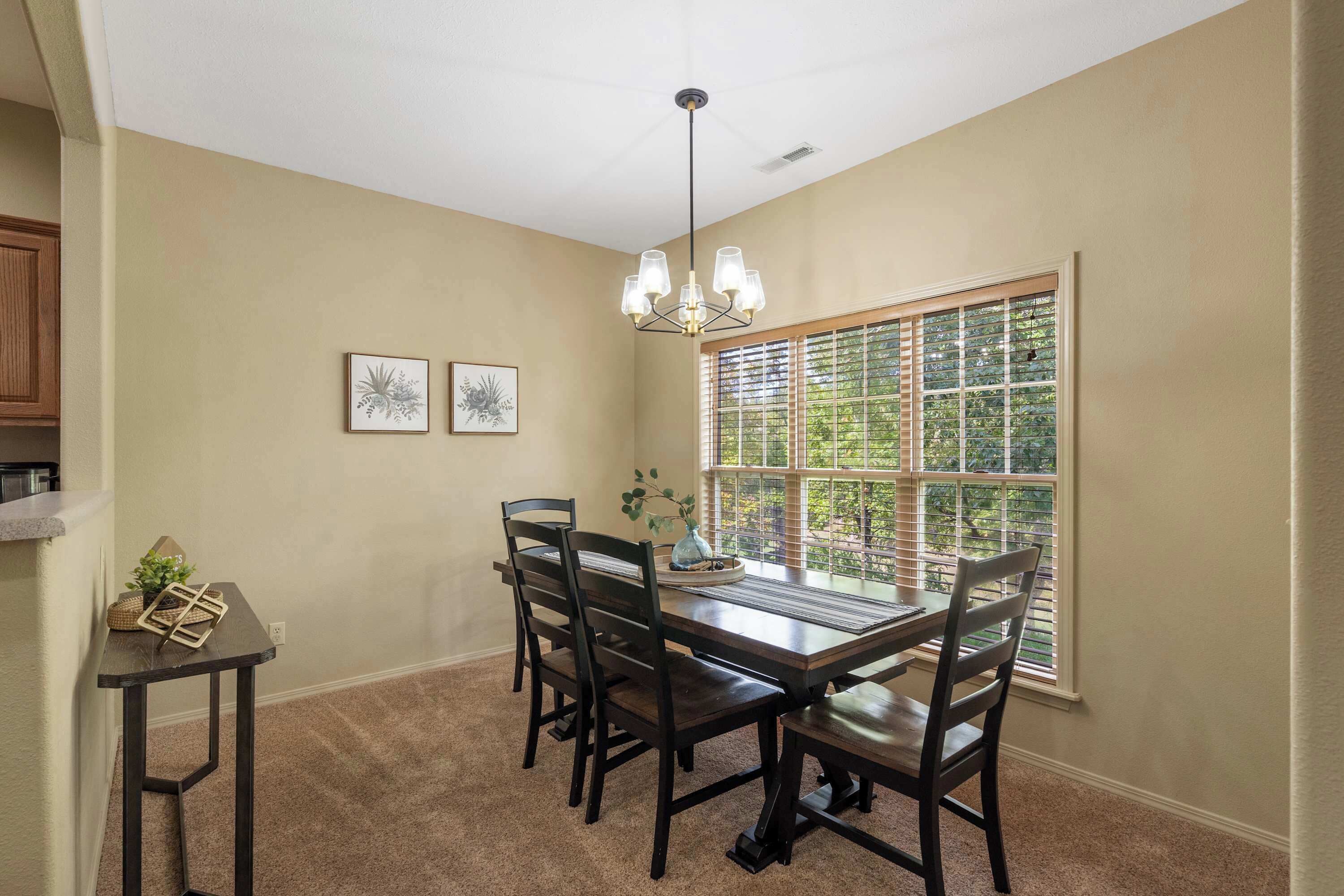 A dining area with a table and chairs, a chandelier, and a window with blinds.