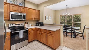A kitchen with wooden cabinets, stainless steel appliances, a dining area with a table and chairs, and a window with blinds. - The Fairway Getaway For 6 (Branson West)
