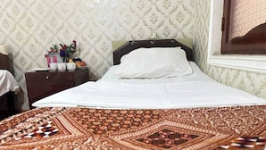 A neatly made bed with a patterned bedspread, a bedside table with a vase of flowers, and a patterned wallpaper in the background. - Iceri iki (Baku)