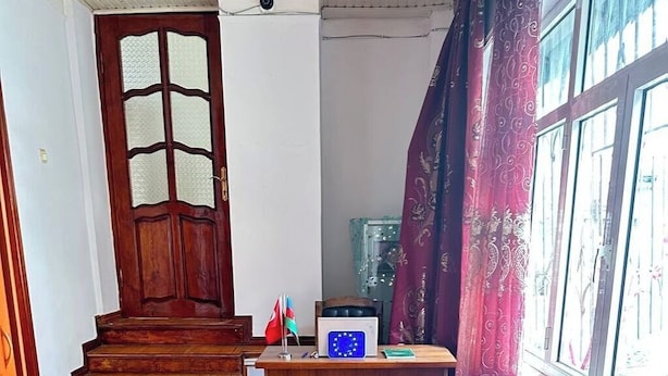 A room with a wooden staircase, a desk with a flag, a window with curtains, and a patterned floor. - Iceri iki (Baku)