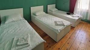 A room with three single beds, a wooden floor, and an air conditioning unit on the wall. - Iceri iki (Baku)