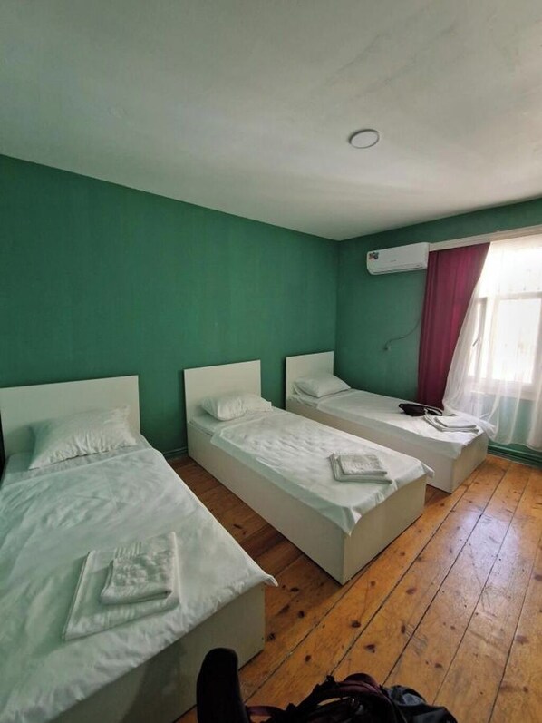 Una habitación con tres camas individuales, piso de madera y un equipo de aire acondicionado en la pared.