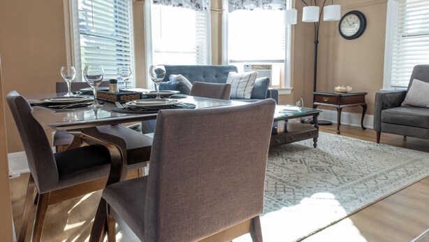 Uma sala de jantar com mesa posta para quatro pessoas, um sofá azul e uma poltrona cinza.