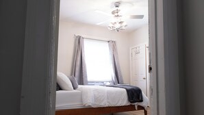 Quarto com cama, ventoinha no teto e janela com cortinas.