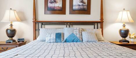 Una cama bien tendida con ropa de cama estampada, dos cuadros colgados en la pared y lámparas de noche a cada lado.