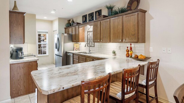 A kitchen with wooden cabinets, a marble countertop, and a breakfast bar with chairs. - R&L Scenic Views Retreat for 4 (Branson)