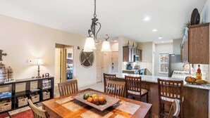 A dining area with a wooden table, chairs, and a fruit centerpiece. There is a kitchen in the background with cabinets and appliances. - R&L Scenic Views Retreat for 4 (Branson)