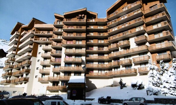 Um hotel com vários andares e varandas, com uma pista de esqui ao fundo e neve no chão.