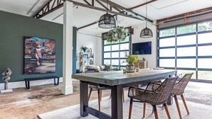 A dining area with a wooden table and wicker chairs, a painting on the wall, and large windows. - Historic 4-BR Loft near Ivy House | Saugatuck (Saugatuck)