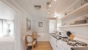 Une cuisine compacte avec des meubles blancs, une cuisinière, un four à micro-ondes et un coin repas comprenant une table et des chaises en bois.