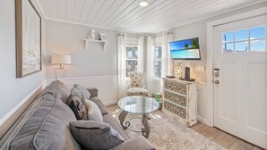 Un salon avec un canapé, une table basse en verre, un téléviseur et une porte.