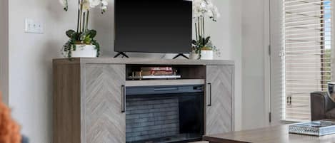 A modern living room with a flat-screen TV mounted above a fireplace, flanked by two white orchid plants.