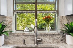 A bathroom with a marble countertop, a modern faucet, and a window with a view of trees. - Fairway Follies Luxury Retreat (Branson West)