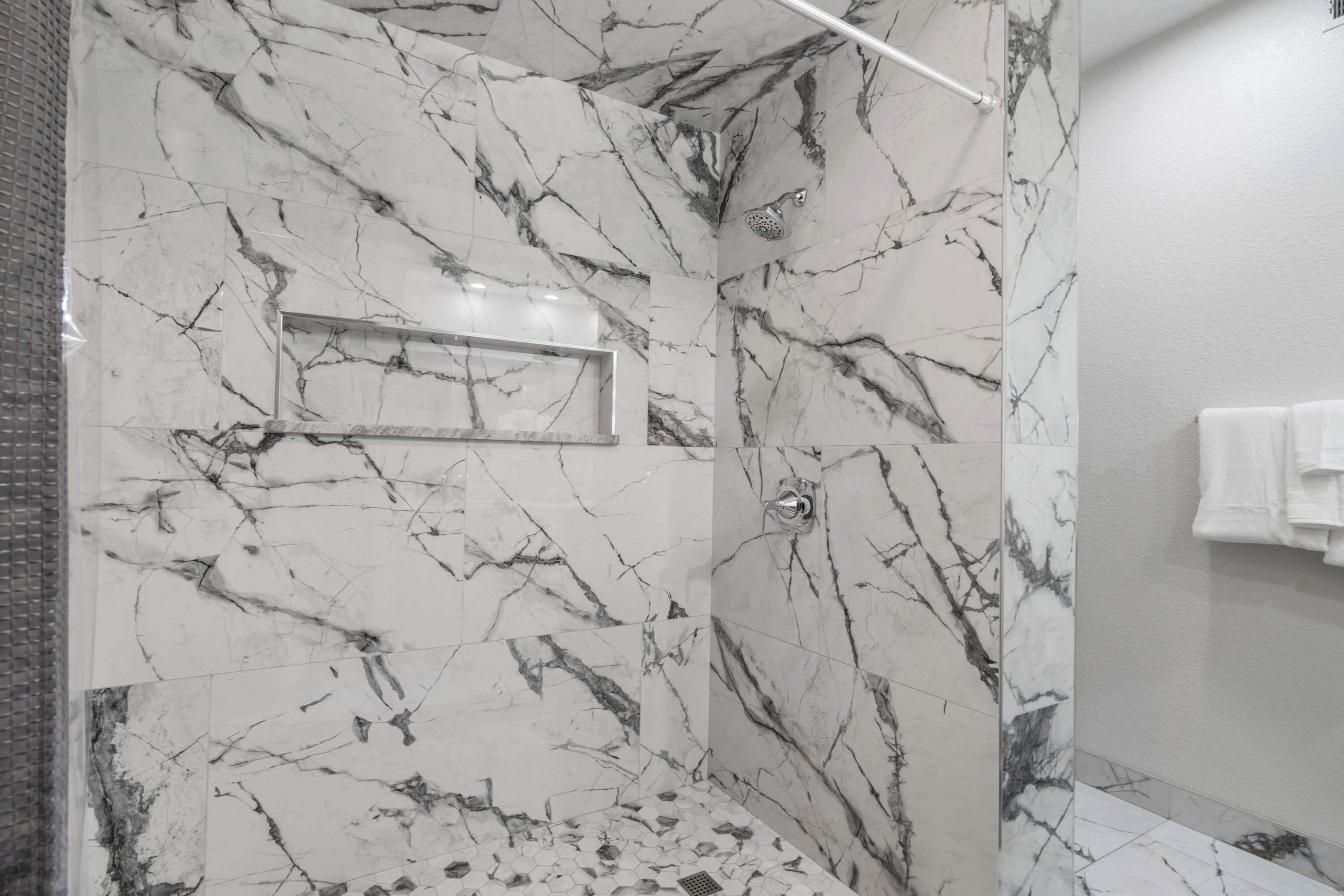A modern bathroom with marble walls and a shower area.