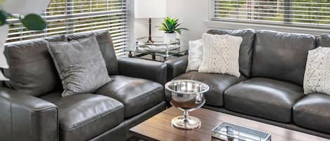 A modern living room with a grey leather sofa, a wooden coffee table, and a metal tray.